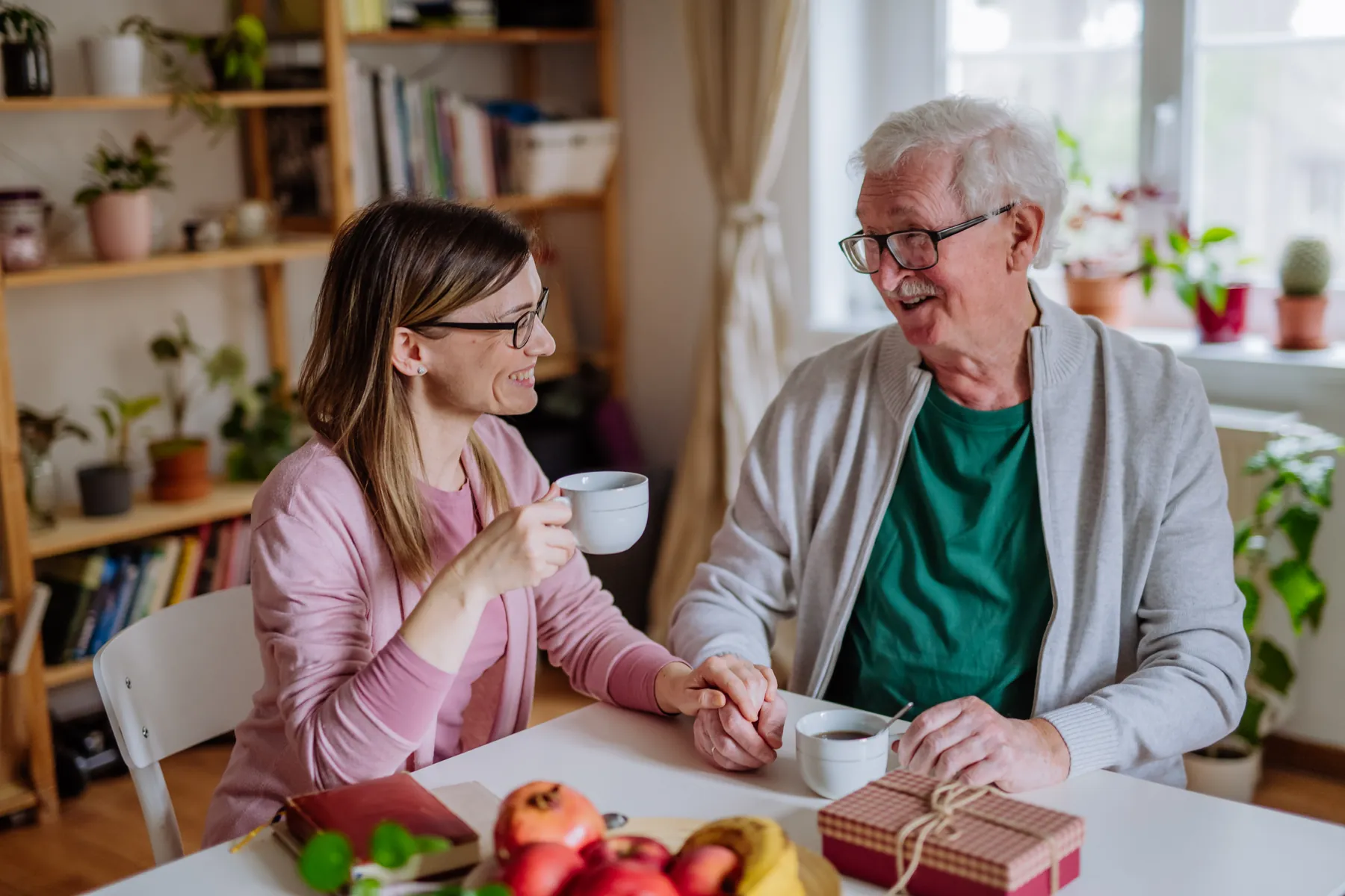 A grown-up daughter having coffee with her father at his home, her hand on his