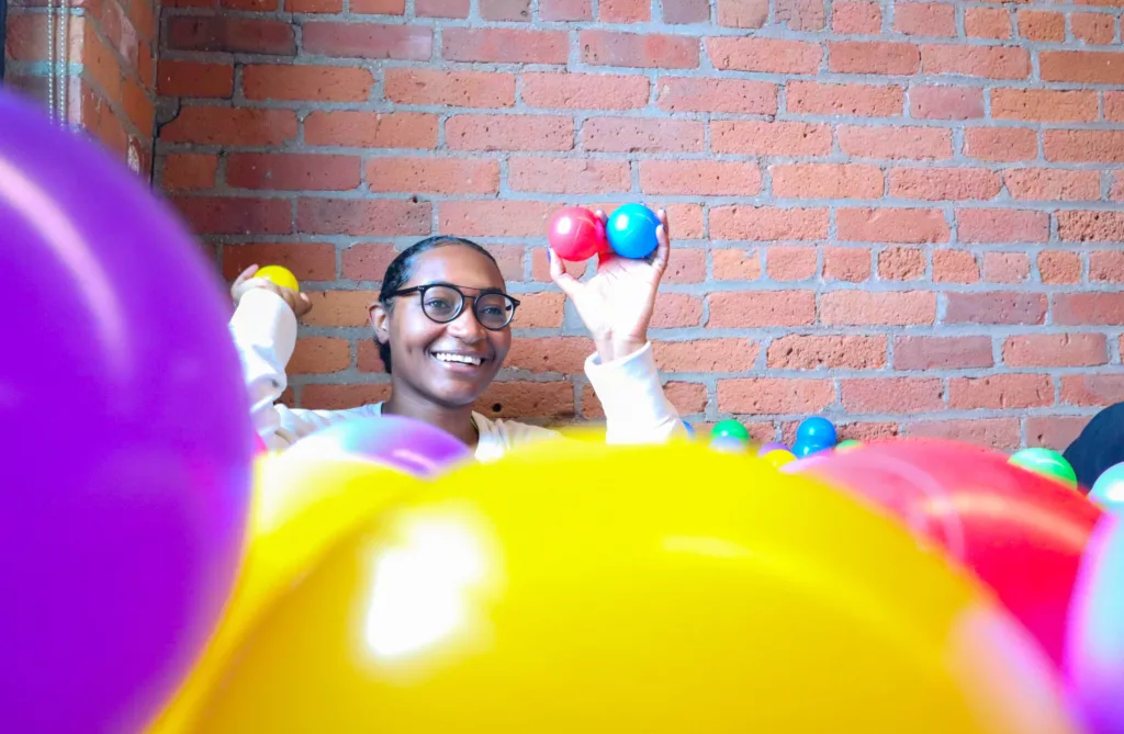 A girl in a ball pit, smiling, throwing balls