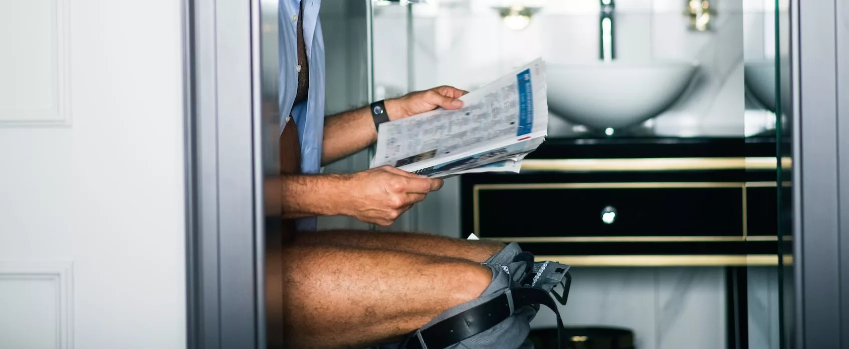 a man sitting on the toilet reading a newspaper