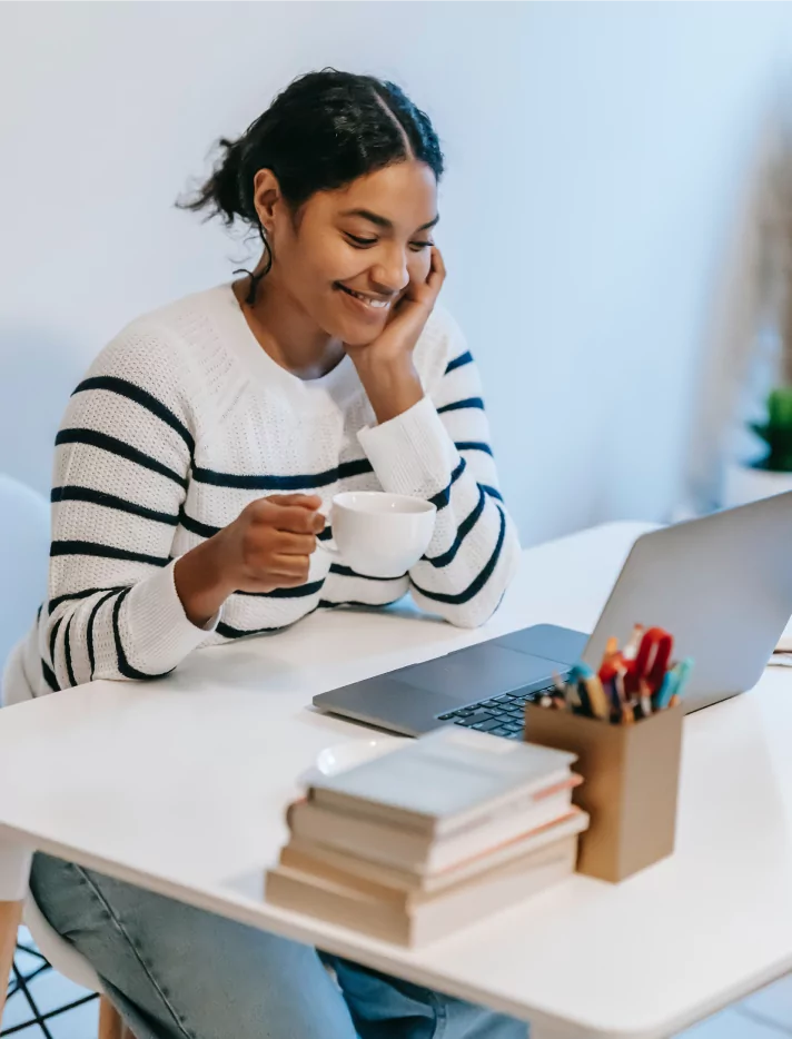 Woman sitting at a laptop, holding a cup of coffee and smiling