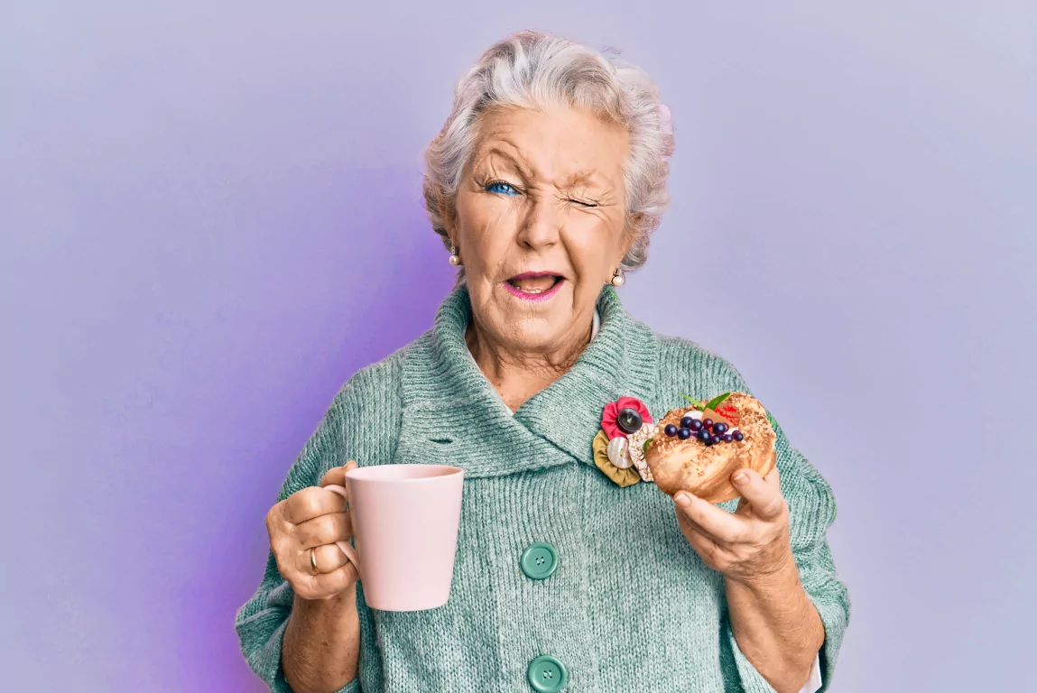 An elderly woman enjoying a cup of coffee and a donut.